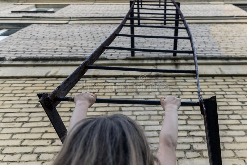 Barn som flickan hänger på den brandflykt som är kopplad till byggnadsfaran för höjder för barn arkivbild Barn som flickan hänger på den brandflykt som är kopplad till byggnadsfaran för höjder för barn arkivbild