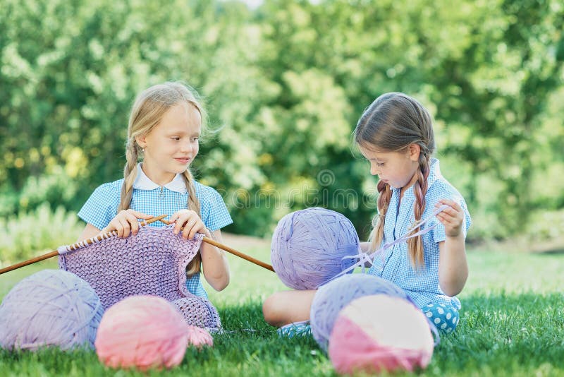 Barn som sitter på gröngräs och trikå med nålar på sommardagen arkivfoto