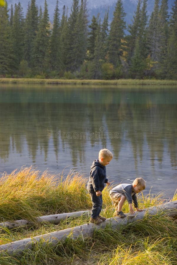 Two children play outdoors on logs near a calm river (Bow River near Canmore, Alberta, Canada). Two children play outdoors on logs near a calm river (Bow River near Canmore, Alberta, Canada)