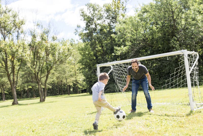Barnet avlar med hans lilla son som spelar fotboll på fotbollgraden royaltyfri fotografi Barnet avlar med hans lilla son som spelar fotboll på fotbollgraden royaltyfri fotografi