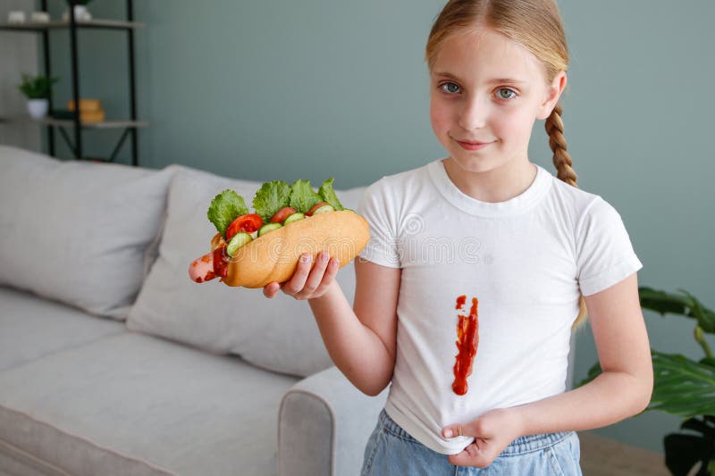 The child stained his clothes with ketchup. A girl eats a hot dog. The child stained his clothes with ketchup. A girl eats a hot dog.