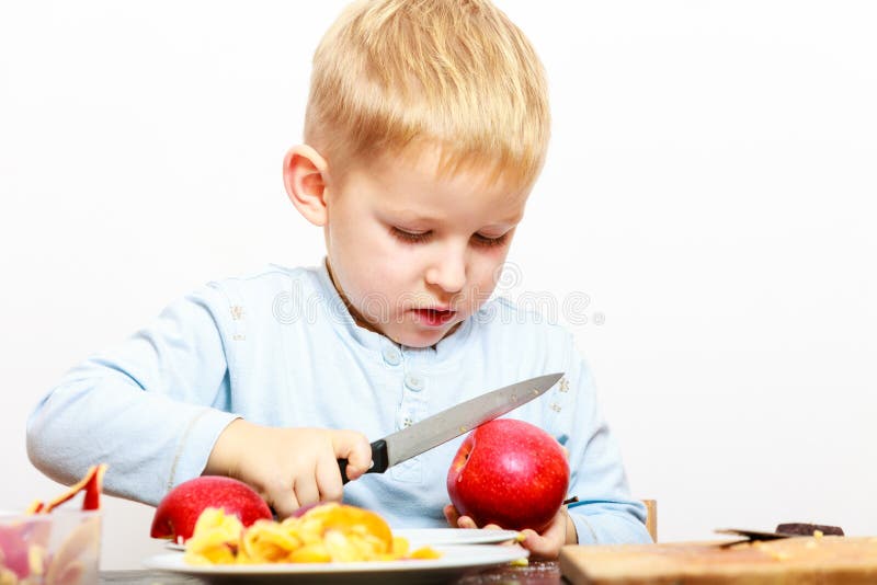 Child little boy playing dangerous game with a kitchen knife cut apple, making salad at home. Child little boy playing dangerous game with a kitchen knife cut apple, making salad at home.