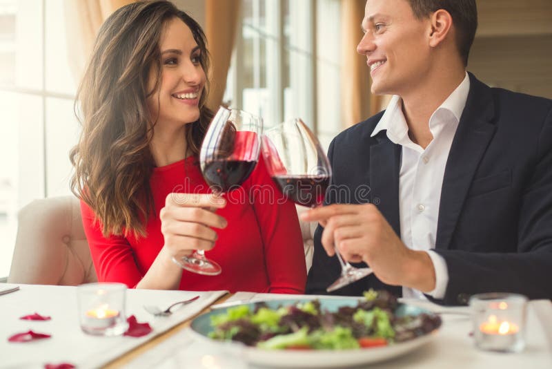 Barnet kopplar ihop att ha den romantiska matställen i restaurangen som sitter rymma tillsammans främre sikt för vinexponeringsgl fotografering för bildbyråer Barnet kopplar ihop att ha den romantiska matställen i restaurangen som sitter rymma tillsammans främre sikt för vinexponeringsgl fotografering för bildbyråer