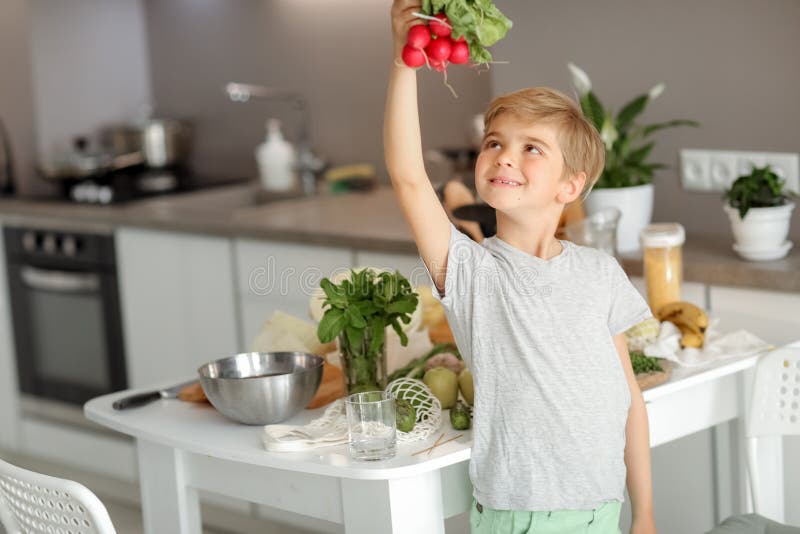 Barnet lägger grönsaker på bordet och bereder en sallad arkivbilder
