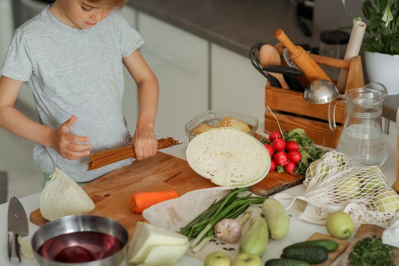 Barnet lägger grönsaker på bordet och bereder en sallad royaltyfri bild
