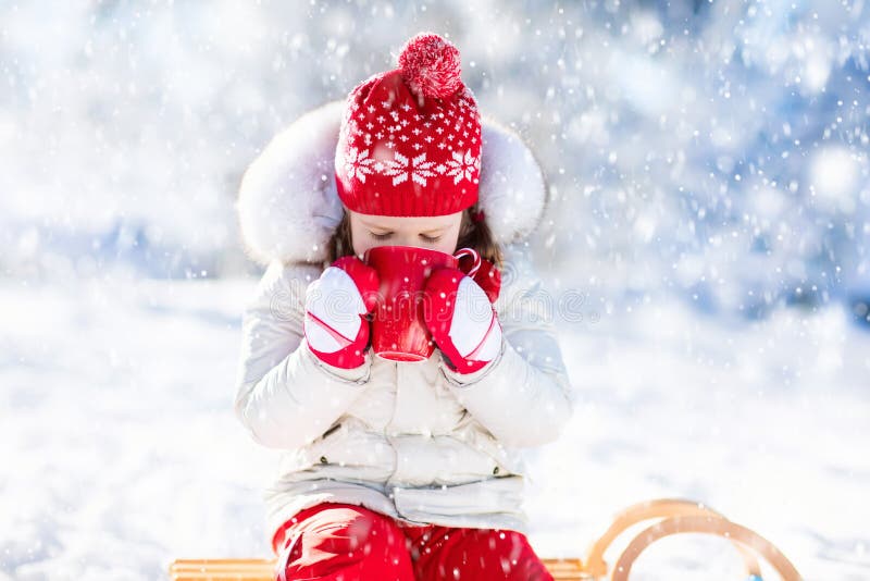 Child drinking hot chocolate with marshmallows in snowy winter park. Kid with cup of warm cocoa drink on Christmas vacation. Little girl playing in snow on Xmas eve. Family outdoor winter fun. Child drinking hot chocolate with marshmallows in snowy winter park. Kid with cup of warm cocoa drink on Christmas vacation. Little girl playing in snow on Xmas eve. Family outdoor winter fun.