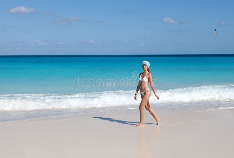 Barnet suntanned den spensliga kvinnan med ett långt ganska hår i den vita sexuella bikinin går på en peschenny strand mot turkosh royaltyfri bild Barnet suntanned den spensliga kvinnan med ett långt ganska hår i den vita sexuella bikinin går på en peschenny strand mot turkosh royaltyfri bild