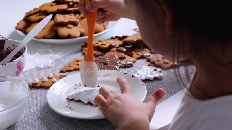 Barnflicka dekorerar xmas-trädformad kaka med vit isbildning genom kulinär pensel