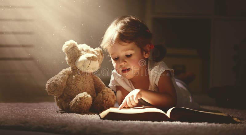 Barnliten flicka som läser en magisk bok i mörkerhem