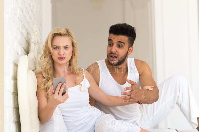 Barnpar Sit In Bed, kvinna som använder problem för latinamerikansk man för cellSmart telefon frustrerat arkivfoton Barnpar Sit In Bed, kvinna som använder problem för latinamerikansk man för cellSmart telefon frustrerat arkivfoton