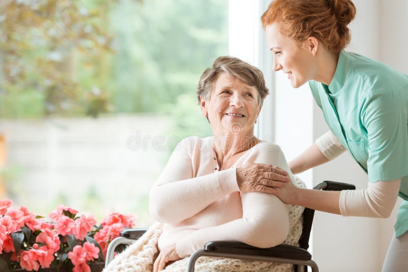 Young nurse helping an elderly women in a wheelchair. Nursing home concept. Young nurse helping an elderly women in a wheelchair. Nursing home concept