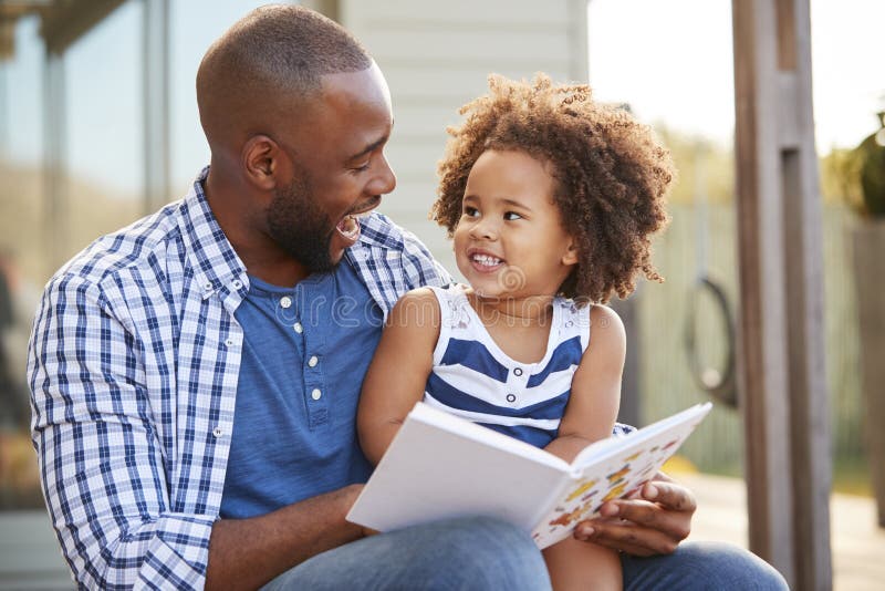 Young black father and daughter reading book outside. Young black father and daughter reading book outside