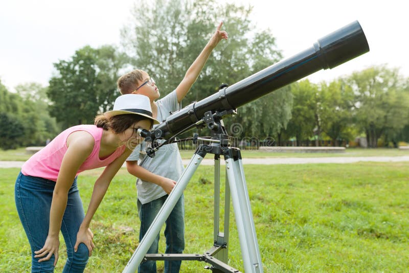 Barntonåringar i parkera som ser till och med ett teleskop fotografering för bildbyråer Barntonåringar i parkera som ser till och med ett teleskop fotografering för bildbyråer