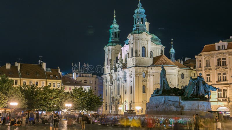 Baroque St. Nicholas&#x27; Cathedral on the Oldtown Square in Prague with monument Jan Hus illuminated at night timelapse. Tourists walk around