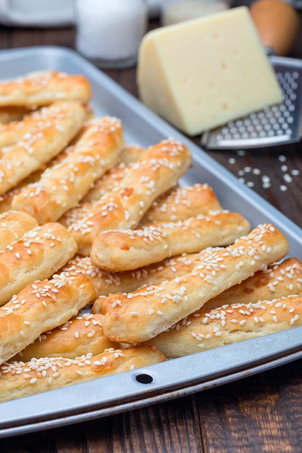 Barras de pan sabrosas hechas en casa con queso y sésamo en la bandeja que cuece, vertical foto de archivo libre de regalías
