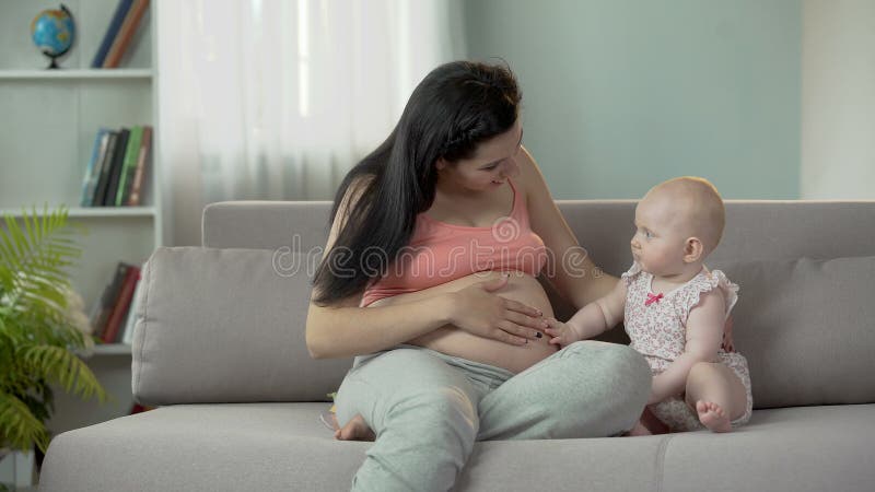 A barriga grávida da mamã tocante do bebê curioso, esperando a irmã mais nova ou o irmão