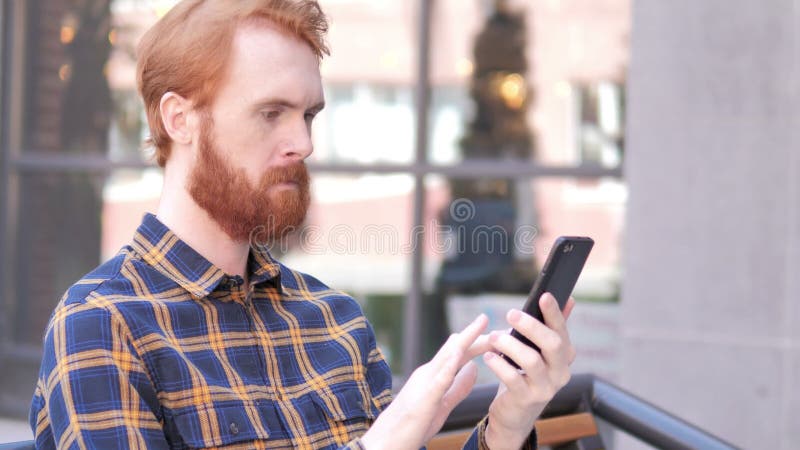 Bart-junger Mann unter Verwendung Smartphones beim Sitzen im Freien