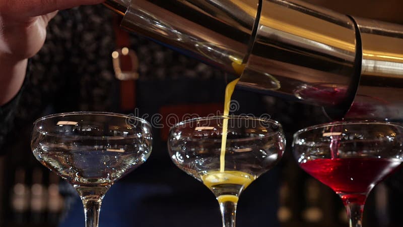 Bartender hands pouring three colored cocktails simultaneously - close up