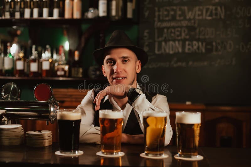 Bartender in Hat with a Beard at Bar Counter with Beer in Glasses Stock