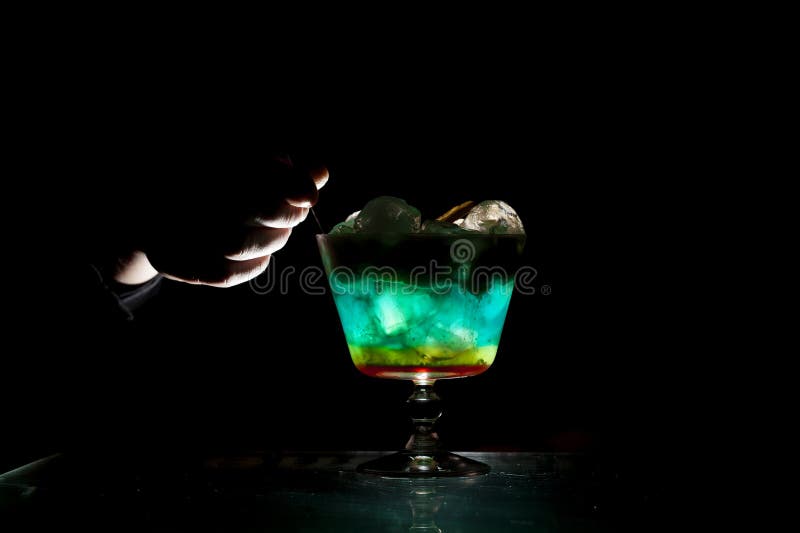 Bartender makes a multi-colored cocktail with ice and foam in a glass on a black background, hands hold the drink royalty free stock image Bartender makes a multi-colored cocktail with ice and foam in a glass on a black background, hands hold the drink royalty free stock image