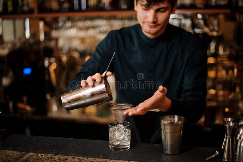 Bartender pouring an alcoholic cocktail into a glass from a steel shaker. Bartender pouring an alcoholic drink from a steel shaker into a cocktail glass with an royalty free stock images Bartender pouring an alcoholic cocktail into a glass from a steel shaker. Bartender pouring an alcoholic drink from a steel shaker into a cocktail glass with an royalty free stock images