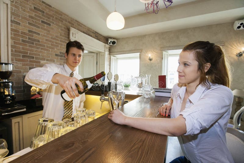 Bartender Pouring Wine for Female Customer at Restaurant Counter Stock