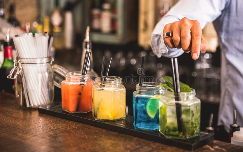 Bartender hand at multicolored fashion drink with straw on vintage glass cups in fashion cocktail bar - Food and beverage concept with professional barman working at mixology restaurant. Bartender hand at multicolored fashion drink with straw on vintage glass cups in fashion cocktail bar - Food and beverage concept with professional barman working at mixology restaurant