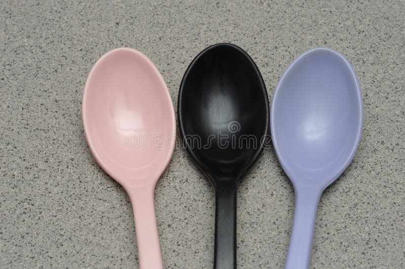 A photo taken on three melamine ware spoon heads with colors purple, black and pink against a granite backdrop. A photo taken on three melamine ware spoon heads with colors purple, black and pink against a granite backdrop..