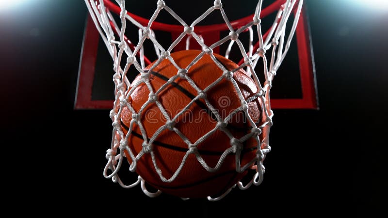 Baschet care trece prin coș pe fundal negru stock photos