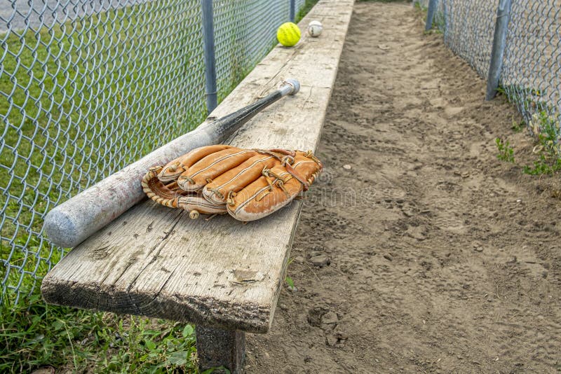 Baseball bat glove and balls on a wood bench in a park