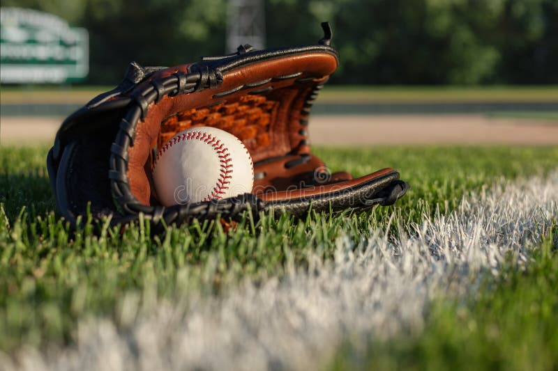 Baseball and mitt selective focus low angle on field with fence and scoreboard royalty free stock photography