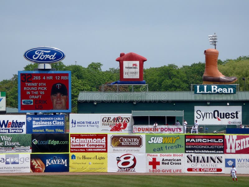 Baseball player stands in the outfield with ads on wall including LL Bean, Ford, Subway, Dunkin Donuts