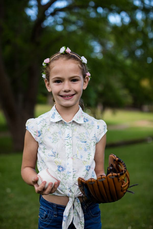 Baseball sveglio della tenuta della ragazza in parco immagine stock Baseball sveglio della tenuta della ragazza in parco immagine stock