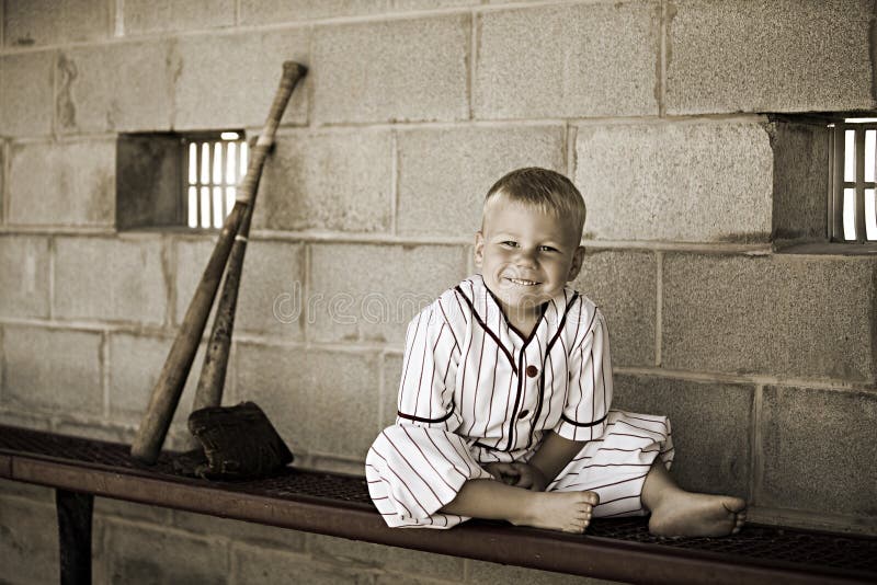 Adorable preschooler dressed in a vintage baseball uniform in a dugout. Desaturated color to give the image a vintage feel. Adorable preschooler dressed in a vintage baseball uniform in a dugout. Desaturated color to give the image a vintage feel.