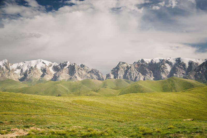 At-Bashi Mountain peaks with snow, green pastures under stormy sky in Kyrgyzstan