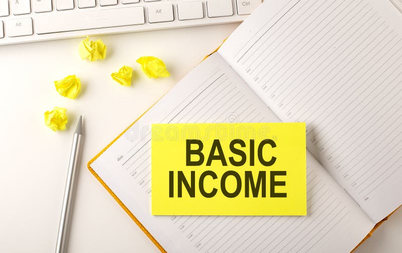 BASIC INCOME text on sticker on the diary with keyboard and pencil stock photo