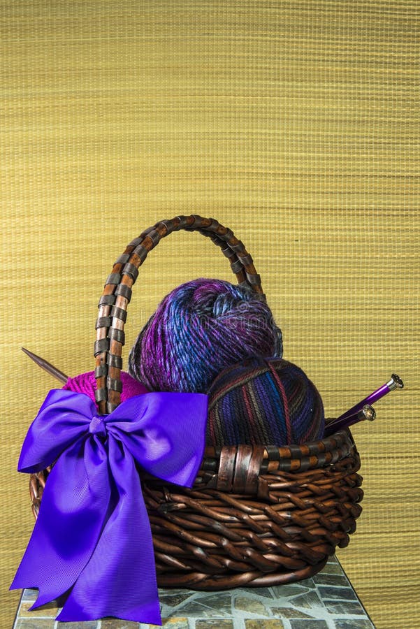 Multicolored yarn balls in a straw basket on a wooden table Stock