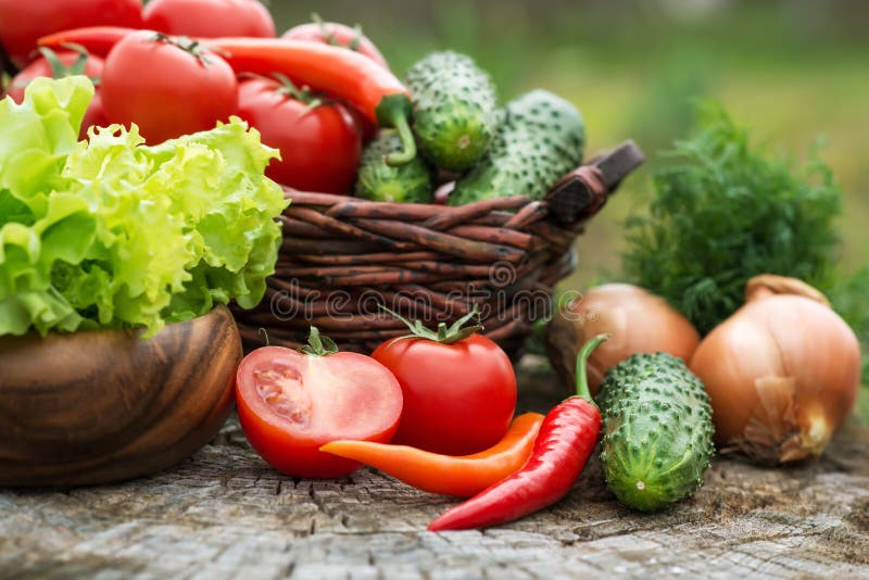 Basket and wooden plate with fresh vegetables (tomatoes, cucumber, chili pepers, dill and lettuce) on wooden background.