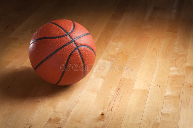 Basketball on hardwood court floor with spot lighting