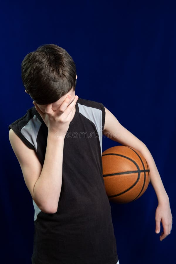 Basketball player. Ball in hand. Failure or frustration in a sports game. A teenager in a black T-shirt covered his face with his