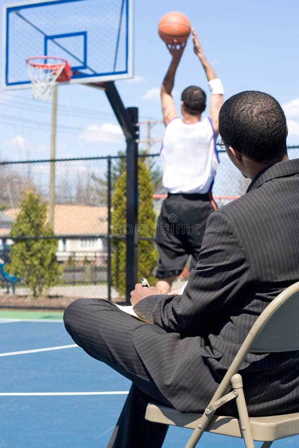 A basketball coach in a business suit observing a player on the team. He could be also be recruiter trying to scout him. A basketball coach in a business suit observing a player on the team. He could be also be recruiter trying to scout him.