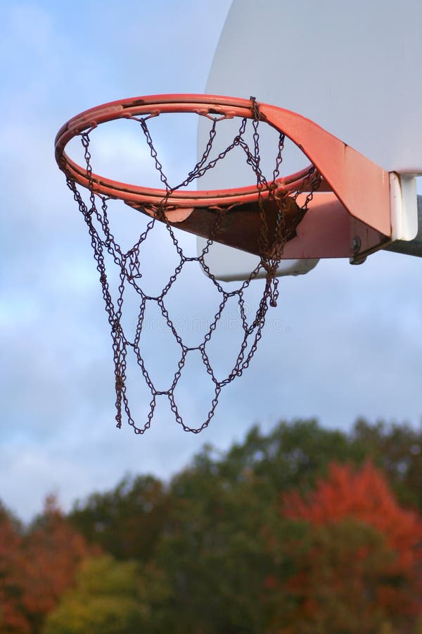 Closeup of basketball backboard and hoop on outside court, against background of autumn trees. Vertical format. Closeup of basketball backboard and hoop on outside court, against background of autumn trees. Vertical format.
