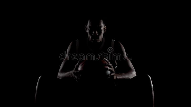 Basketbollspelare som sitter på bänk. Koncentrerad afrikansk amerikansk idrottsman mot svart bakgrund. arkivfilmer