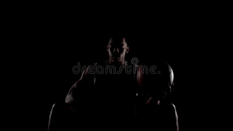 Basketbollspelare som sitter på en bänk och ber. Religiös amerikansk idrottsman mot svart bakgrund. arkivfilmer