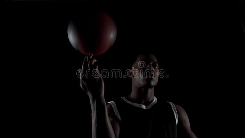 Basketbollspelare som snurrar en boll. Amerikansk idrottsman som utövar mot svart bakgrund. arkivfilmer