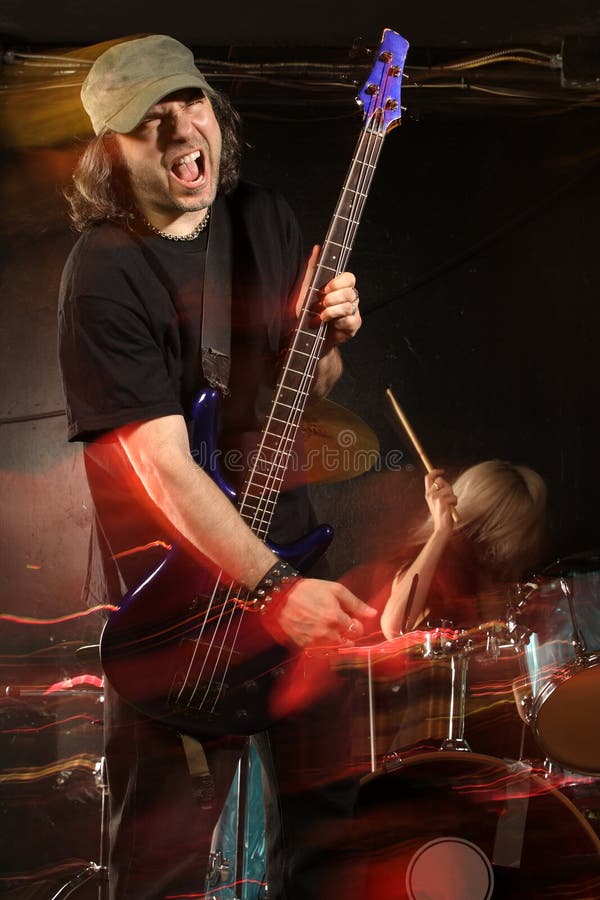 Bass player playing on a stage with female drummer. Shot with strobes and slow shutter speed to create lighting atmosphere and blur effects. Motion blur on performers. Bass player playing on a stage with female drummer. Shot with strobes and slow shutter speed to create lighting atmosphere and blur effects. Motion blur on performers.