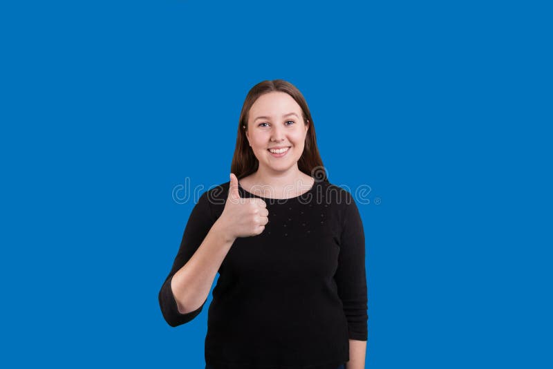 Bastante donante de la señora pulgares encima de la sonrisa dulce en fondo azul imágenes de archivo libres de regalías Bastante donante de la señora pulgares encima de la sonrisa dulce en fondo azul imágenes de archivo libres de regalías