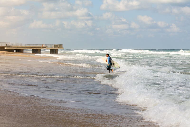 Bat Yam, Israel - 14 July, 2014. Young surfer man going out of the water in stormy weather royalty free stock photography Bat Yam, Israel - 14 July, 2014. Young surfer man going out of the water in stormy weather royalty free stock photography