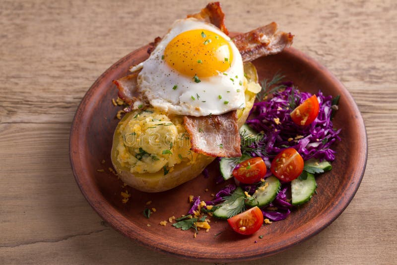 A batata cozida no revestimento carregou com o queijo e cobriu com bacon e ovo frito na placa com vegetais Batata enchida com top fotografia de stock royalty free A batata cozida no revestimento carregou com o queijo e cobriu com bacon e ovo frito na placa com vegetais Batata enchida com top fotografia de stock royalty free