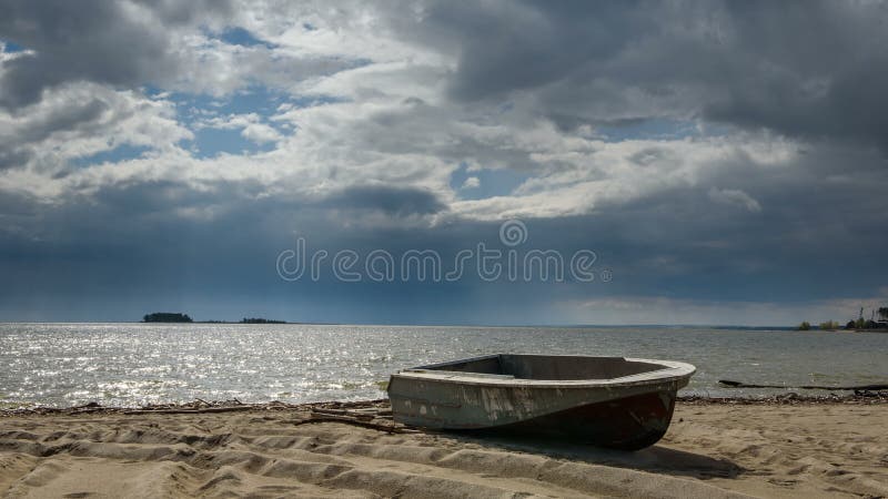 Bateau de pêche se situant dans le sable sur le rivage du lac, nuages fonctionnant à travers le ciel il n'y a personne autour